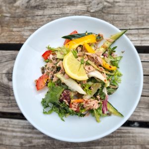 Tuna Salad with cucumber, peppers and salad leaves on white plate on wooden picnic bench background.