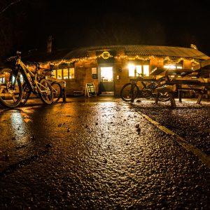 Frontage of Pedalabikeaway Cafe in dark lit with fairy lights along the front and mountain bikes parked outside either side.