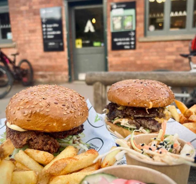 Two burgers, one beef, one chicken, with fries and sides of Korean slaw, photo taken in front of the Pedalabikeaway Cafe