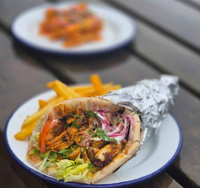 A chicken wrap filled with fresh lettuce, onion, tomato and spiced chicken with a side of fries