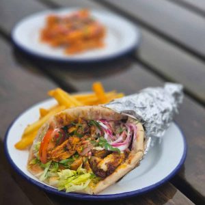 A chicken wrap filled with fresh lettuce, onion, tomato and spiced chicken with a side of fries