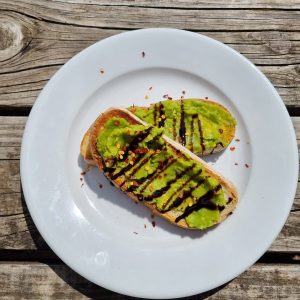 Avocado on Sourdough Toast drizzled with balsamic vinegar on white plates and wooden picnic bench background