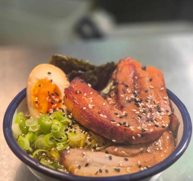 A bowl of ramen topped with meat, egg, seaweed and spring onions
